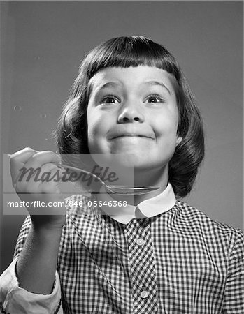 1960s GIRL WITH SMILING YUMMY FACIAL EXPRESSION HOLDING SPOON
