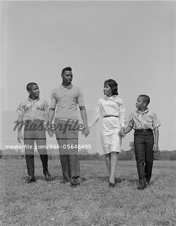 1960s AFRICAN-AMERICAN FAMILY HOLDING HANDS WALKING IN GRASSY FIELD