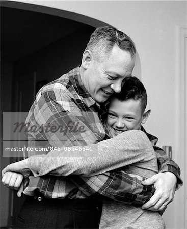 1950s - 1960s SMILING FATHER AND SON HUGGING INDOOR