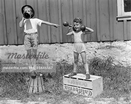 ANNÉES 1930 - ANNÉES 1940 GARÇONS JOUANT CARNAVAL STRONGMAN UN LEVAGE HALTÈRES AUTRE LOI ANNONÇANT AU MÉGAPHONE