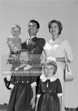 1960s PORTRAIT SMILING FAMILY FATHER MOTHER TWO DAUGHTERS SON STANDING TOGETHER OUTDOORS