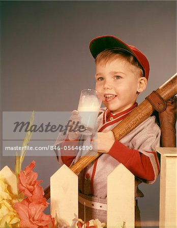 FÜNFZIGER JAHRE - SECHZIGER JAHRE JUNGE TRINKEN MILCH TRAGEN BASEBALL UNIFORM VON LATTENZAUN