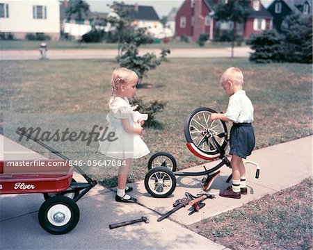 1950ER JAHRE BLONDE MÄDCHEN SISTER HOLDING PÜPPCHEN BEOBACHTEN KLEINE JUNGE BRUDER REPARATUR DREIRAD