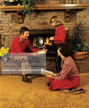 1970s - 1980s FAMILY FATHER MOTHER DAUGHTER SITTING BY FIREPLACE POPPING CORN