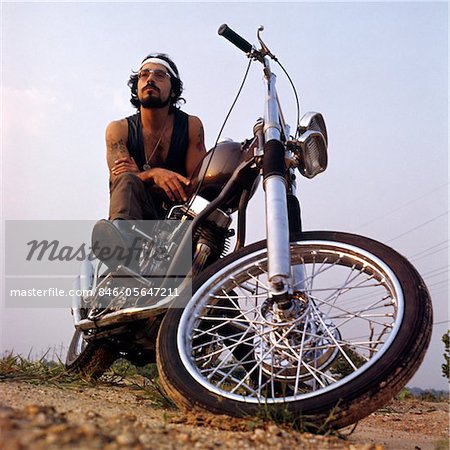 1970s TATTOOED BEARDED MAN SITTING ON CHOPPER MOTORCYCLE