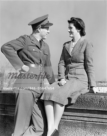 ANNÉES 1940 COUPLE HEUREUX HOMME ARMÉE UNIFORME FEMME ASSISE SUR LE MUR DE PIERRE