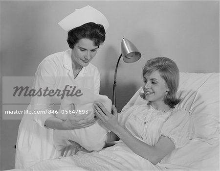 1960s WOMAN NURSE GIVING BABY TO SMILING MOTHER PATIENT SITTING IN HOSPITAL BED