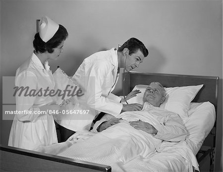 1960s DOCTOR AND NURSE CHECKING ON ELDERLY MALE PATIENT IN HOSPITAL BED