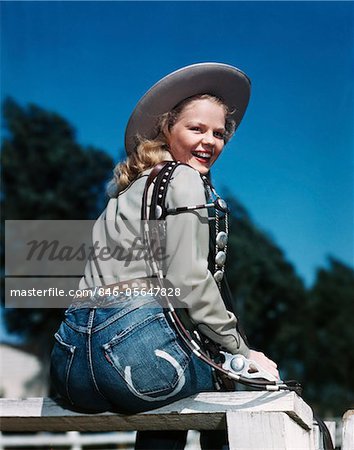 1940s - 1950s SMILING BLOND WOMAN WEARING WESTERN COWGIRL CLOTHES LOOKING OVER SHOULDER SITTING ON WOODEN FENCE