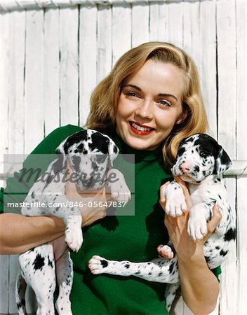 1950s PORTRAIT SMILING TEEN GIRL WEARING GREEN SWEATER HOLDING TWO DALMATIAN PUPPIES