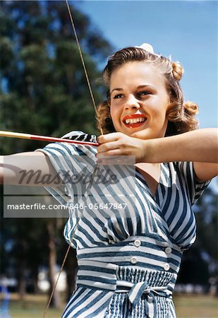 1940s - 1950s SMILING TEEN GIRL ARCHER WEARING BLUE AND WHITE STRIPED DRESS SHOOTING AIMING BOW AND ARROW