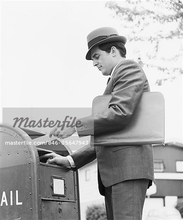 1970s YOUNG BUSINESSMAN WITH BRIEFCASE DROPPING LETTER INTO MAILBOX