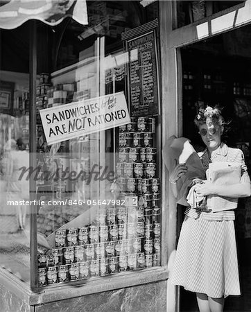 1940s WOMAN CARRYING PACKAGES IN DOOR OF NEW YORK CITY DELICATESSEN DISPLAYING A SIGN SANDWICHES TO TAKE OUT ARE NOT RATIONED