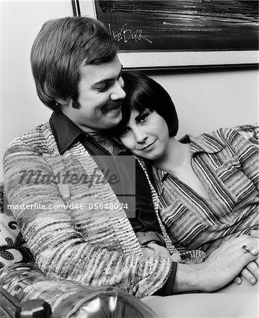 1970s ROMANTIC COUPLE MAN WOMAN HUGGING SITTING ON SOFA