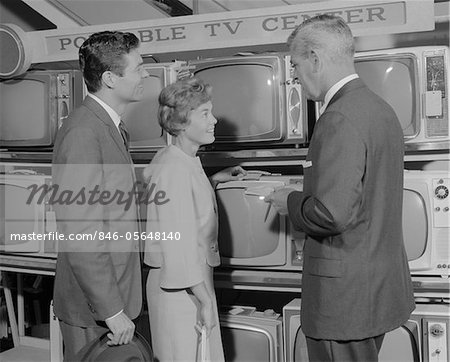 1960s COUPLE SHOPPING FOR PORTABLE TV BEING HELPED BY SALESMAN