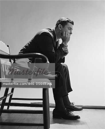1960s SAD MAN RESTING HAND ON CHIN SITTING ON BENCH