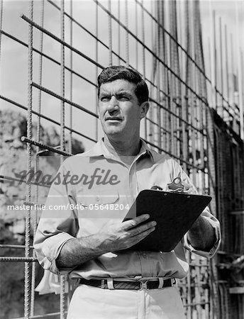 1960s MAN ON CONSTRUCTION SITE HOLDING CLIPBOARD