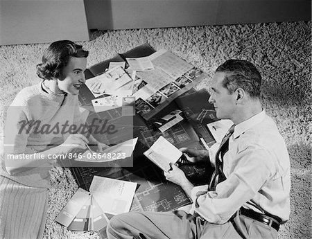 1950s COUPLE MAN WOMAN SITTING FLOOR LOOKING AT PLANS FOR NEW HOUSE