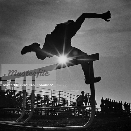 1970s SUN RAYS THROUGH SILHOUETTE OF MAN JUMPING TRACK FIELD HURDLE