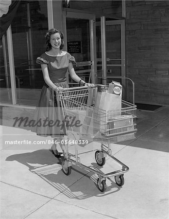 1950s SMILING WOMAN PUSHING GROCERY CART OUT OF SUPERMARKET