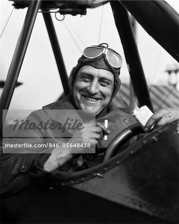 1920s SMILING MAN PILOT IN COCKPIT OF AIRPLANE LOOKING AT CAMERA TAKING CIGARETTE OUT OF PACK