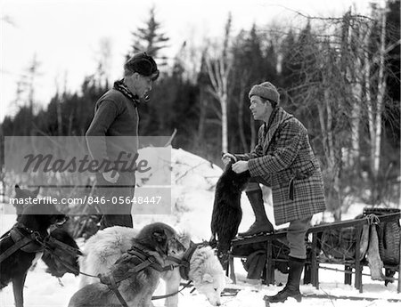 1920s - 1930s TWO MEN FUR TRAPPERS STANDING BY TEAM OF SLED DOGS
