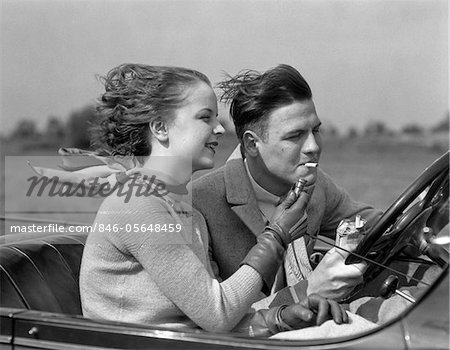 1930s MAN DRIVING CONVERTIBLE AUTOMOBILE WHILE GIRLFRIEND LIGHTS HIS CIGARETTE