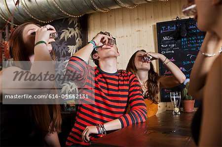Young friends drinking from shot glass in bar