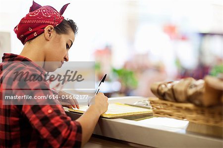 Jeune femme écrivant sur le comptoir de la boulangerie