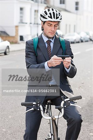 Mid adult businessman using cellphone to text on bicycle