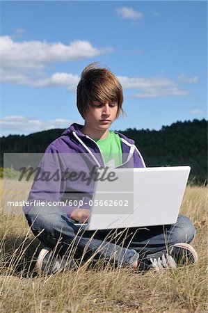 Boy Sitting in Field using Laptop Computer, Blandas, Gard, France