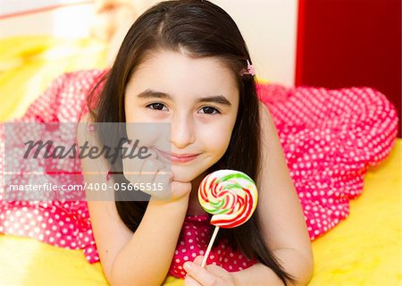 Little girl with lollipop in her bedroom.