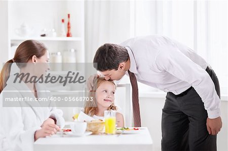 The father kisses his daughter before leaving the kitchen