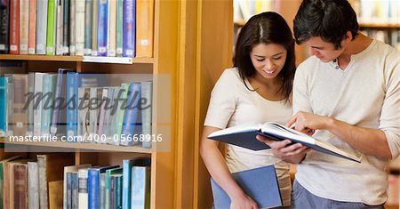 Smiling students looking at a book in a library