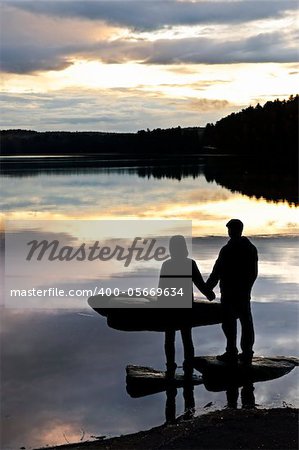 Sun setting over tranquil lake with people watching in silhouette