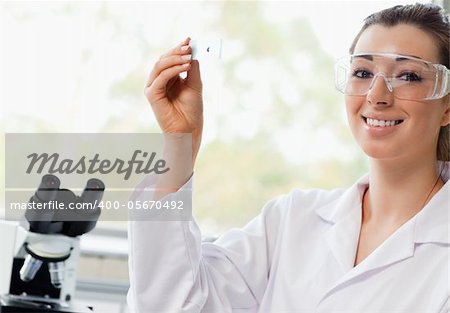 Smiling science student holding a microscope slide in a laboratory