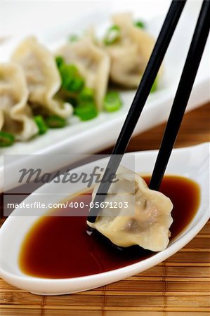 Dumpling being dipped in soy sauce with chopsticks