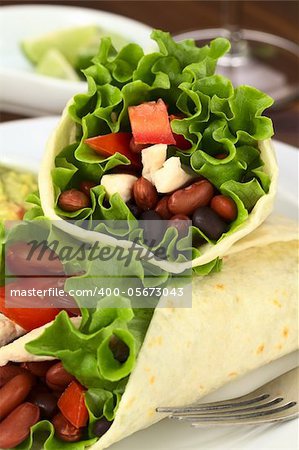 Mexican tortilla wraps filled with chicken, beans, tomato and lettuce (Selective Focus, Focus on the stuffing of the upper wrap)