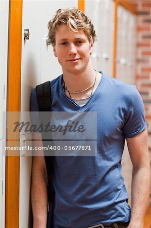 Portrait of a smiling student leaning on a locker in a corridor