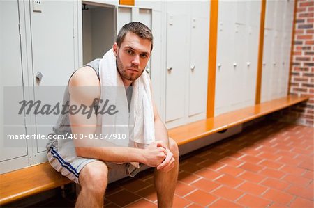 Handsome young sports student sitting on a bench with a towel