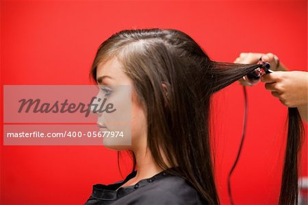 Woman having her hair straightened against a red background