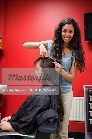 Portrait of a happy female hairdresser cutting hair with scissors