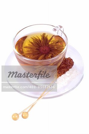 Transparent cup of Chinese tea in the form of decorative flower and two sticks with decorative - white and brown sugar on white background.