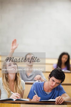 Student raising his hand while his classmates are taking notes in an amphithater