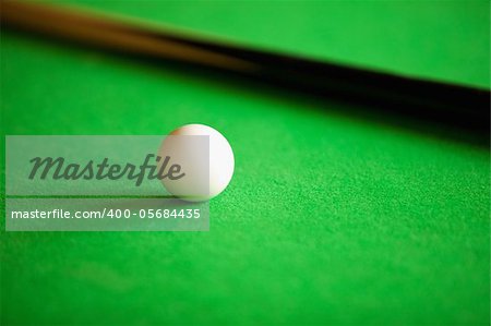 Close up of a queue ball and a queue against a green background