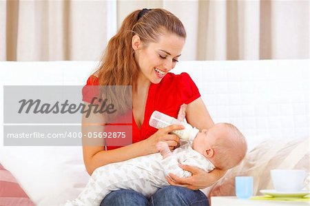 Happy mother sitting on sofa and feeding baby