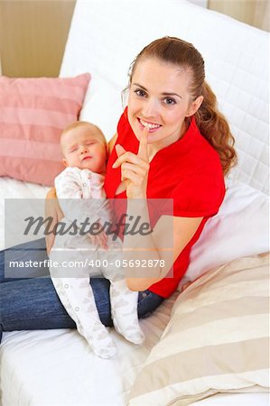 Happy mother holding sleeping baby and showing shhh gesture