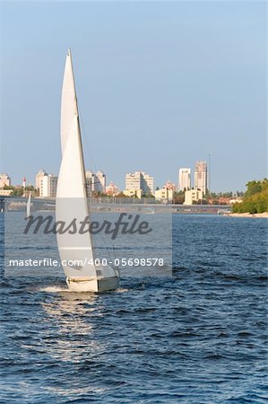 Vessel ship with white sails on water with urban scene as background