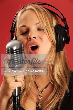 Photo of a beautiful young blond wearing headphones and singing into a vintage microphone.