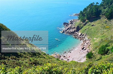 Secluded beach with a boat in the clear blue sea. Steep cliffs covered with vegetation surround the beach making a hidden cove.